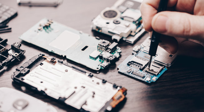 Person repairing electronic circuit boards with tools on a wooden table.