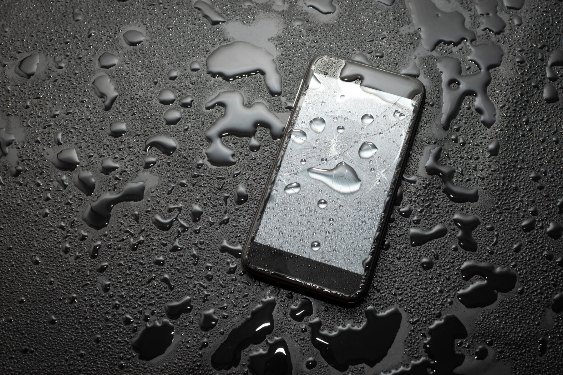 Wet smartphone lying on a dark surface with water droplets, highlighting water-resistant phone features.